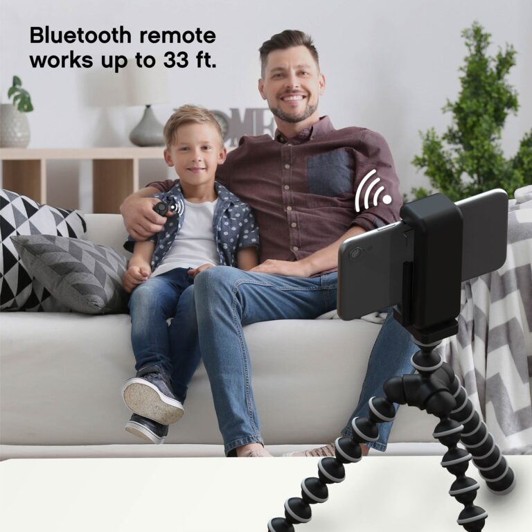 A young man and his son sitting on the couch together and using the Bluetooth shutter remote to take a selfie with the tripod.